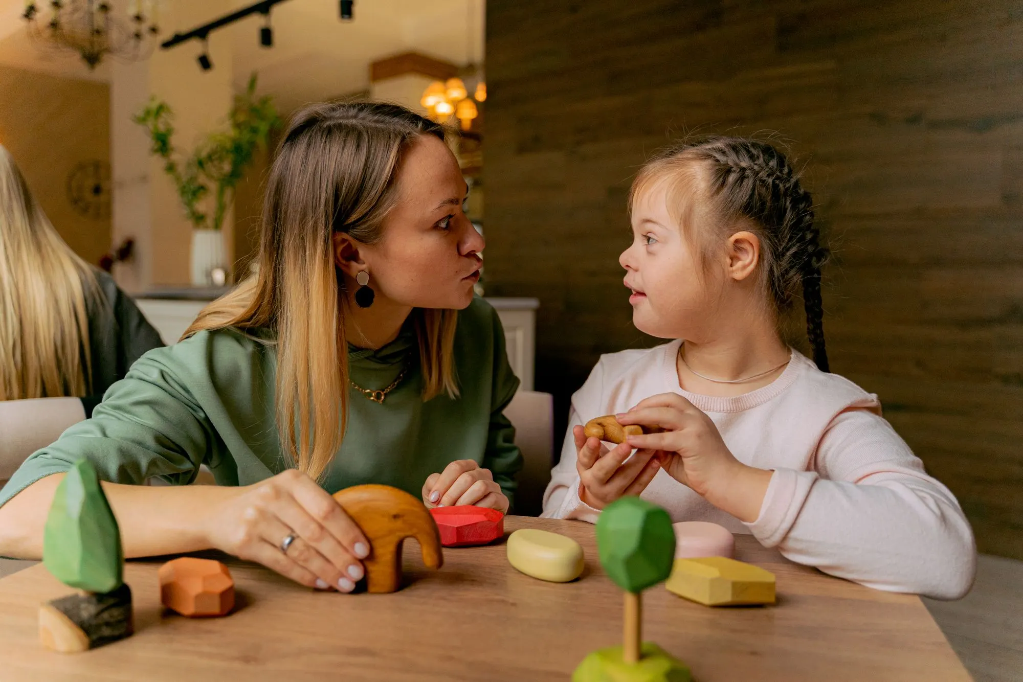 Adulta e criança sentadas à mesa a brincar com peças de madeira coloridas